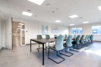 Lichte modulaire kantoorruimte met vergadertafel, stoelen en ramen.