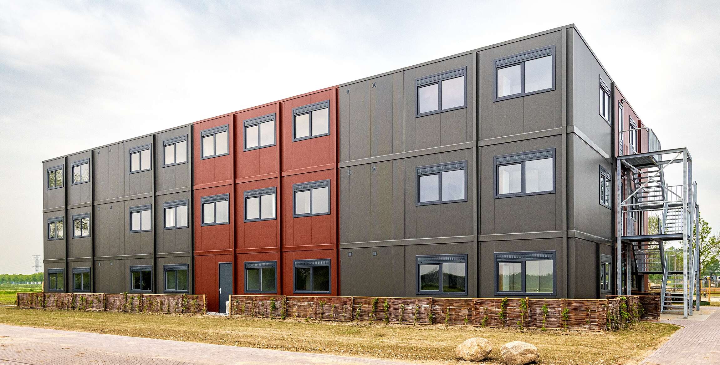 Modulaire woonunits in rood en grijs op een verzorgd terrein.